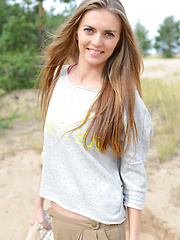 Erotic picture of Delicious teen beauty undressing and spreading her long shapely legs outdoors on the sand.