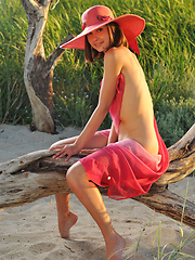 Erotic picture of Enchanting girl in a hat with a wide brim showing her perfect body outdoor on the coast.